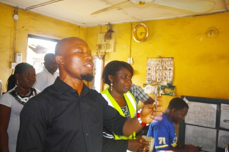 In his shop in Akwa Ibom, Nigeria, Bassey Ngehaji stands next to Mama Condom and prays while holding up a condom. Photo by Chika Oduah