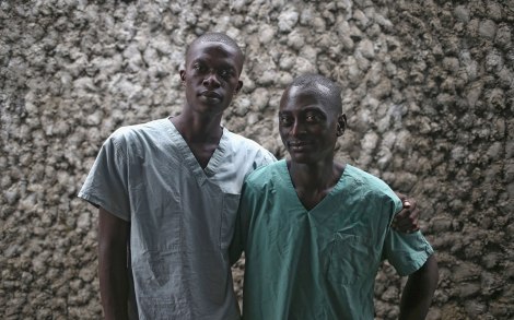 Ebola survivors Mark Jerry, 30, (R), and Zaizay Mulbah, 34, stand together before their shifts as nurse's assistants at the Doctors Without Borders (MSF), Ebola treatment center on October 12, 2014 in Paynesville, Liberia. Jerry was a money changer and Mulbah a delivery driver before they caught the disease and went to the MSF center where they recovered. MSF hired them afterwards to counsel and comfort others stricken by the disease. Ebola kills about 70 percent of the people it infects, according to the World Health Organization, but leaves survivors immune to the strain that sickened them. (Photo by John Moore/Getty Images)