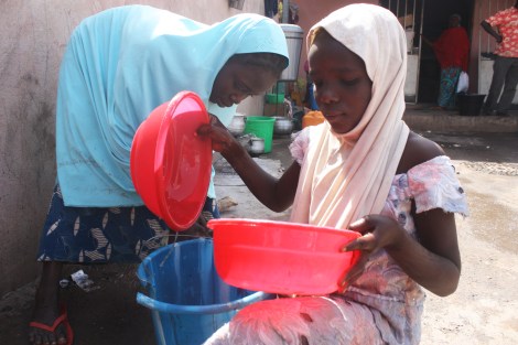 11-year old Hauwa Marshall gathers water, Fatimatu, 14, washes dishes behind her. They were orphaned when Boko Haram fighters killed their father a few weeks ago. Now, they live in his refugee camp in Yola in northeastern Nigeria. January 17. Photo by Chika Oduah