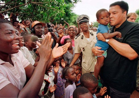 Former heavyweight boxing champion Muhammad Ali kisses a Liberian orphan while residents cheer Ali's arrival at an orphanage for Liberian refugees in San Pedro, Ivory Coast. Ali and his entourage came on a goodwill visit to donate food, wheelchairs, and medicine after receiving a letter asking for help from the mission's organizer Sister M. Sponsa Beltran. Aug. 20, 1997 (AP Photo/David Guttenfelder)