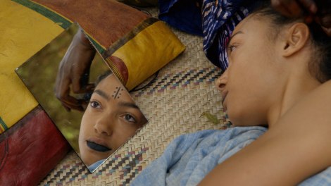 Tiyaa, the main character, looks in the mirror as a woman combs her hair. 